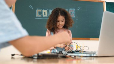 Kız tornavida kullanarak elektronik tahtayı tamir ederken ayakta duruyor. Amerikalı öğrenci ve beyaz çocuk elektrik sistemini denetlemek için birlikte çalışıyorlar. Gemide çalışan meraklı çocuklar. Pedagoji.