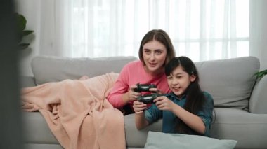 Annem kanepede yatarken, mutlu kız oyun oynuyor ve oturuyor. Beyaz bir ebeveyn ve çekici zeki bir kız elinde joystick ile birlikte vakit geçirip maç kazanmaya odaklanıyor. Yaşam tarzı. Pedagoji.