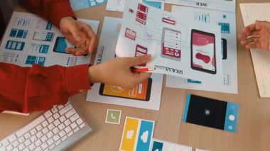 Mobil uygulama için kullanıcı arayüzü prototipini ofis çalışanlarına sunan harika bir şirket çalışanı. UX UI tasarımcısı kağıt üzerinde simge tasarımının işlevini açıklıyor. Sinerjik