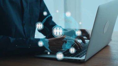 Küresel bağlantıyı temsil eden ve modern iş çözümleri için ağ oluşturan dijital simgelerle çevrili ahşap bir masada dizüstü bilgisayar kullanan bir birey. Dörtgen