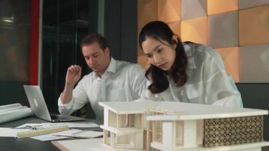 Bir grup mimar mühendis birlikte çalışıyor ve ofis tasarımı hakkında tartışıyorlar. Genç mühendis ev modelini ölçerken yönetici dizüstü bilgisayar kullanıyor. İş tasarımı konsepti. Yönlendirici.