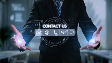 Profesyonel bir işadamı ellerini modern bir ofiste uzatarak, dijital temas seçeneklerini kusursuz iletişim için kullanabileceği sanal bir arayüz üzerinden sunuyor. Dörtgen