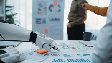 Robotik bir el modern ofis ortamında iş çizelgeleriyle uğraşır, veri analizlerinde teknoloji ve insan işbirliğinin kesişimini gösterir. Noogenesis