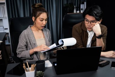 Stresli suratlı iki yönetici birlikte evrak işlerini tartışıyorlar. Modern ofiste gece geç saatlerde dizüstü bilgisayarla karşılaştırıldığında şirket projesinde çalışıyorlar. İnfobahn.