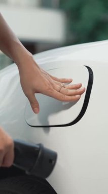 İlerici kadın evdeki elektrikli aracına şarj istasyonu fişi takıyor. EV otomobilleri çevreye yararlı temiz ve yeşil enerji kavramı sağlar.