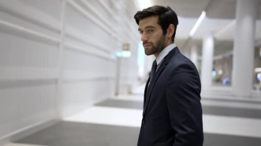 Beyaz arkaplan ile alışveriş merkezinde dikilirken kameraya bakan gülümseyen iş adamı. İş elbisesi giyerken kameraya gülümseyen başarılı adamın yakın çekimi. Mutlu yönetici kameraya bak. Sevinçli..