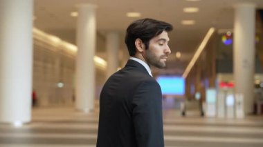 Profesyonel bir iş adamı kolları bağlıyken arkasını döner. Kafkasyalı mutlu yatırımcı, arka planı bulanık bir şekilde koridorda kollarını kavuştururken kameraya özgüvenle bakıyor. Portre. Sevinçli..