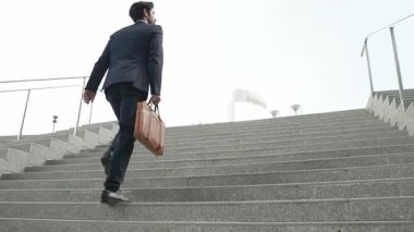 Akıllı bir iş adamının elinde çantayla merdivenlerden yukarı çıkışının en üst görüntüsü. Profesyonel proje yöneticisi merdivenlerden çıkıp işyerine gidiyor. Yeteneklerini arttırmak, terfi almak, seyahat etmek. Sevinçli..