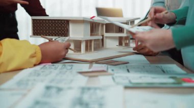 İşbirlikçi bir ekip mimari bir modeli tartışırken, parlak ve modern bir ofis alanındaki plan ve belgeleri gözden geçirir. Yaratıcı etkileşim yenilikçi fikirleri teşvik eder. SACTR