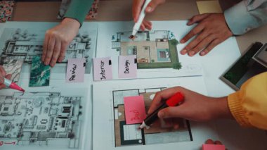 Profesyonellerin çizimler, renkli kalemler ve notlarla çevrili ortak bir tasarım sürecine girdiklerini gösteren canlı bir sahne. Yaratıcı çalışma alanı temaları için ideal. SACTR