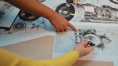 Bu resim mekanik çizimler yapmakla meşgul elleri gösteriyor, profesyonel bir çalışma alanında teknik araçlar ve vitesler, hassasiyet ve yaratıcılığı vurguluyor. SACTR