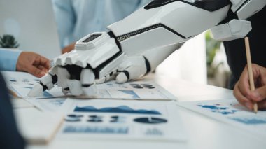 Gösterişli bir robot el, bir toplantı sırasında iş haritaları ve grafikler üzerinde profesyonellerle işbirliği yaparak, iş yerindeki teknolojinin entegrasyonunu vurguluyor. Noogenesis