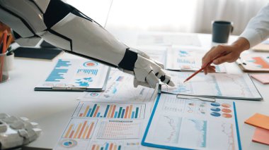 Bir insan ve robotik kol veri tabloları ve raporlarla dolu bir tablo üzerinde etkileşime girerek, teknolojinin iş analizi ve takım çalışmasına entegrasyonunu vurguluyor.