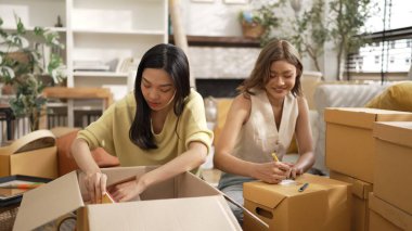 Çekici bir oda arkadaşı oturma odasında paket paketlerken pakette konum yazıyor. Mutlu satıcı birlikte çalışıyor ve teslimat paketini hazırlıyor. Girişimci kargo kutusu paketliyor. Myrmidon.