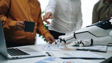 Dinamik bir ofis sahnesi kahve, çizelge ve belgelerle insanlar ve robotlar arasındaki etkileşimi gösteriyor, teknolojide işbirliğinin geleceğini gösteriyor. Noogenesis