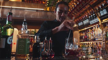 Zeki Asyalı barmen bardakta karıştırılmış alkol şurubunu buzla karıştırıyor. Çünkü kayanın üzerinde kamera var. Gece kulübünde taze kokteyl kokteylleri karıştırıyor. Vinosity.