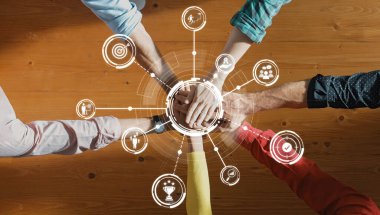 Takım çalışmasını, yenilikçiliği ve başarı ve bağlılığı temsil eden dijital simgelerle çevrili, çeşitli ellerin bir masanın üzerinde birleştiği dinamik bir sahne. Dostluk