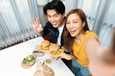 Gülümseyen ev sahibi aşçıların akıllı telefonuyla fotoğraf çekerken üst görüntüsü yemek programında çift hamburger tutarken sosyal medya kanalında ev yapımı salata tabağıyla kolaylıkla görülebiliyor. İnfobahn.