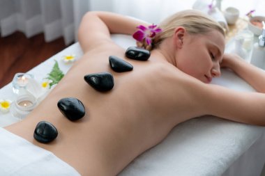 Lüks tatil köyündeki kaplıcalarda sıcak taş masajı. Gün ışığı sükunet ortamında, mutlu kadın müşteri bazalt taş masajından zevk alıyor. Rahatlatıcı bir sıcaklıkla vücudun üzerinde süzülüyor. Sessiz.