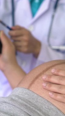 Mutlu hamile kadın, jinekolog doktoru hastanede ya da klinikte hamilelik danışmanlığı için ziyaret ediyor. Doktor, bebek ve anne sağlığı kontrolü için hamile karnı muayene ediyor. Jinekoloji konsepti.