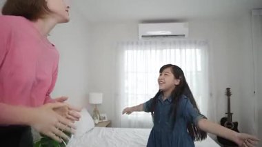Yatak odasında Asyalı kızıyla müzik eşliğinde dans eden mutlu çekici anne. Beyaz anne dans eder ya da egzersiz yapar. Bu arada tatlı çocuk da müzik eşliğinde yatağa atlar. Aile eğlence konsepti. Pedagoji.