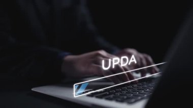 Bir dizüstü bilgisayarda dijital güncelleme çubuğuyla yazılan ellerin odaklanmış görüntüsü. Karanlık arkaplan, yazılım gelişimini sembolize ederek teknoloji simgelerini geliştiriyor. Dörtgen