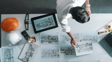 Bina yapısını analiz etmek için dizüstü bilgisayar kullanırken tablete bakan mühendislerin yukarıdan aşağı görüntüsü. Proje planıyla toplantı masasında iç tasarımı kontrol eden mimarın hava görüntüsü. Hizalama.