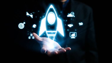 Bir iş adamı elinde yenilik ve başarıyı simgeleyen parıldayan dijital bir roket tutuyor. Çevreleyen ikonlar, hevesli girişimciler için büyüme, hedef ve teknoloji kavramlarını temsil ediyor. Dörtgen
