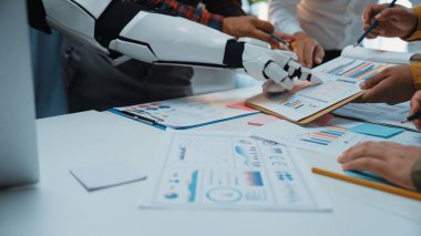 Fütüristik bir ofis sahnesinde çeşitli veri ve çizelgeleri analiz eden, takım çalışmalarını ve yeniliklerini geliştiren bir grup uzmana yardımcı olan robotik bir kol sergileniyor.