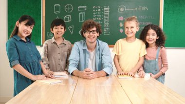 Profesyonel Kafkas öğretmeni ve çeşitli öğrenciler kameraya bakarken mutlu okul çocuğu gülümsüyor. Sınıfın önünde dururken gülümseyen bir grup çok kültürlü çocuk. Eğitim. Pedagoji.