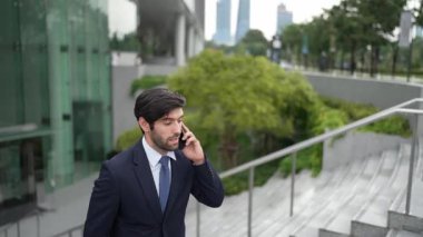 Gülümseyen yakışıklı iş adamı, parkın merdivenlerinde yürürken aynı zamanda işletme müdürünü arıyor. Yatırımcı işe giderken meslektaşıyla konuşuyor. Sevinçli..