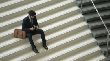 Akıllı bir iş adamının iş planı yapmak için telefon ve dizüstü bilgisayar kullanması. Merdivenlerde otururken. Müdür terfi alıyor, bilgisayarla arkadaşlarını ararken satışları arttırıyor. Sevinçli..
