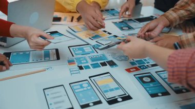 Tasarımcıların kullanıcı arayüzü kavramları üzerinde iş birliği yaptıkları canlı bir sahne, yaratıcılıkla dolu modern bir çalışma alanında fikirler üzerinde beyin fırtınası yaparken eskizler ve cihazlar kullanıyorlar. SACTR