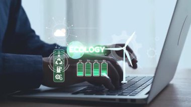 Dizüstü bilgisayarda yazı yazan ellerin yakın plan görüntüsü, rüzgar türbinleri ve pil göstergeleri gibi grafik elementler aracılığıyla ekoloji için yenilikçi teknolojiler sergiliyor, sürdürülebilirliği vurguluyor. Dörtgen