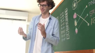 Öğrenciye bakarken, sınıfta matematik teorisi hakkında konuşan ve açıklayan beyaz bir öğretmen. Tahtanın önünde durup tahtaya işaret eden yetenekli bir eğitmen. Pedagoji.