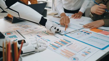 İş yerindeki gelişmiş teknolojiyi tasvir eden eşsiz bir sahne. Robot bir el, insan ekibiyle birlikte detaylı iş verilerini ve stratejilerini analiz ediyor.