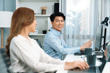 Gülümseyen Asyalı bir adam, yan görüntüdeki modern ofis çalışma masasında veri tabanını ararken günlük dizüstü bilgisayarla pazarlama raporu projesini planlarken kadın meslektaşıyla konuşuyor. İnfobahn.