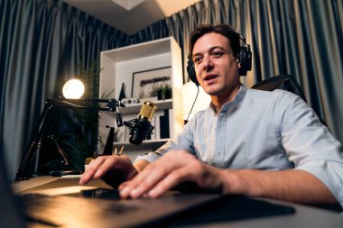 Sunucu kanalı akıllı yayıncı laptopta canlı sosyal medya uygulaması arıyor, kulaklık takıyor ve modern ofis stüdyosundaki mikrofonu kullanıyor. Bireysel.