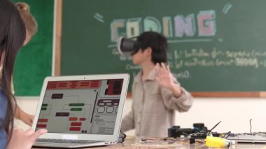 Kız kodlama sistemiyle uğraşırken metaworld 'e elektronik panoyla girmek için VR kulaklık takan bir çocuk. Çeşitli öğrencilerden oluşan bir grup program geliştirmek ve mühendislik kodu yazmak için birlikte çalışıyor. Pedagoji.