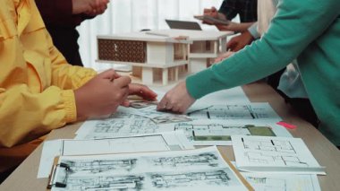 İşbirlikçi bir tasarım sürecinde yer alan bir grup profesyonel, planlar ve mimari modelleri tartışıyor. Sahne, ofis ortamında yaratıcılığı ve takım çalışmasını yakalıyor. SACTR