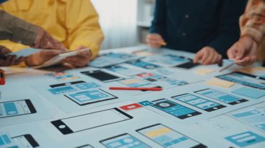 Çeşitli bir ekip akıllı telefonlar ve modeller kullanarak mobil uygulama prototipleri üzerinde işbirliği yapıyor. Sahne, modern çalışma ortamında yaratıcılık ve takım çalışması sergiliyor. SACTR