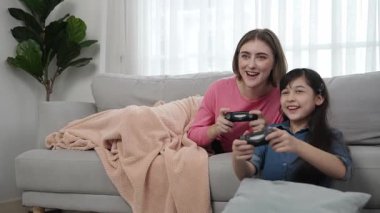 Annem kanepede yatarken, mutlu kız oyun oynuyor ve oturuyor. Beyaz bir ebeveyn ve çekici zeki bir kız elinde joystick ile birlikte vakit geçirip maç kazanmaya odaklanıyor. Yaşam tarzı. Pedagoji.