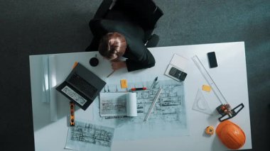 Güvenlik miğferi, cetvel ve ekipmanlarla masada otururken dizüstü bilgisayar kullanarak bina inşaatını analiz eden yetenekli tasarımcının üst görüntüsü. Bilgisayarda çalışan müdürün hava görüntüsü. Hizalama.