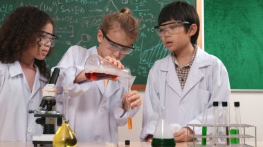 Kafkasyalı öğrenci deney yapıyor ve laboratuvarda yeni yenilikler keşfetmek için bekleyen meraklı çocuklarla çevrili biyokimyasal solüsyon döküyor. Çeşitli mutlu öğrenciler deney yapıyor. Pedagoji.