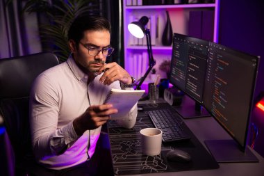 Akıllı bilişim geliştiricisi bilgisayar ekranında yazılım geliştirme kodlaması üzerinde çalışıyor ve en yeni uygulama projesinin notlarını okuyor, program güncellemesi düşünüyor neon ışıklı siber ofiste online web sitesi verileri. Tahmin et..