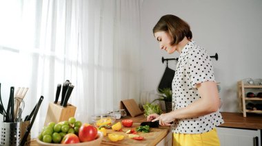 Enerjik anne, mutfak malzemeleri ile çevrili sebzeleri doğrarken modern mutfakta kahvaltı için salata yapıyor. Akıllı kadın temizlikçi yemek pişirir ve yemek hazırlar. Sağlıklı bir yaşam tarzı. Pedagoji.