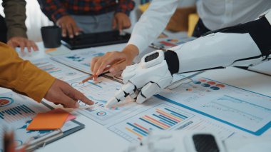 Modern bir ofiste, insanlarla bir robotun veri analiz çizelgeleri üzerinde işbirliği yaptığı takım çalışmasını ve iş bütünleşmesinin geleceğini simgeleyen dinamik bir sahne. Noogenesis