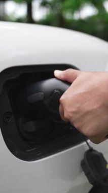 İlerici adam elektrikli aracına elektrik kablosu takıyor. Ev şarj istasyonundan EV arabası. Çevreyi korumak için temiz ve yenilenebilir enerji kullanan elektrikli bir araba. Çevre dostu otomobil.