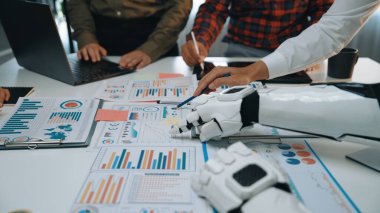 İş ortamlarında yenilik ve üretkenliği vurgulayan veri analiz grafikleri ve araçların yer aldığı modern bir çalışma alanı, insanlar ve robotlar arasındaki işbirliğini sergiliyor.