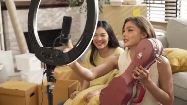 İnternette yayınlanırken gitar kılıfını gösteren ve satan mutlu bir çift. Çekici kız oturma odasında reklam ürünleri için online pazarlama kullanarak yayın yapıyor. Myrmidon.